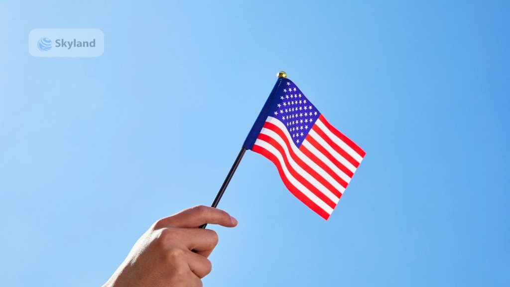 Hand holding a small American flag against a blue sky